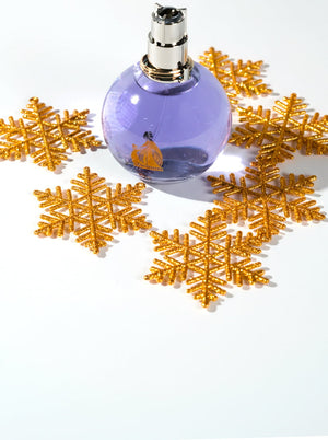 Purple spherical perfume bottle with a silver cap, surrounded by glittery gold snowflakes on a white background — a festive and budget-friendly fragrance option for the holidays.