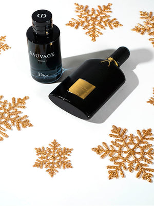 Dior Sauvage and Tom Ford Black Orchid colognes displayed on a white background with festive gold snowflakes, showcasing luxurious holiday fragrance picks.