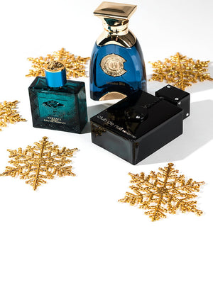 Three bestselling men's fragrances—Versace Eros Eau de Parfum, Milano Blu, and Club de Nuit Intense Man—arranged with festive gold snowflakes, styled for the holiday season.