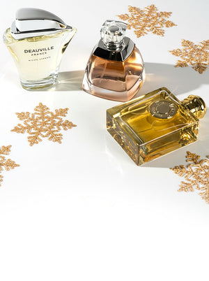 Three popular women's perfumes—Deauville France, Vera Wang, and a golden designer fragrance—displayed with sparkling gold snowflakes for a festive holiday look.