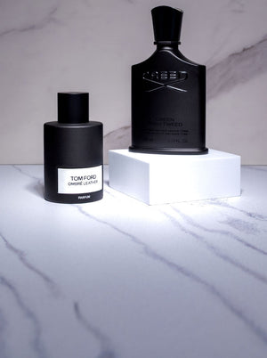Tom Ford Ombre Leather and Creed Green Irish Tweed fragrances displayed on white pedestal blocks against a marble background.