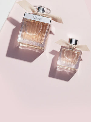 Chloé perfume bottles with ribbon detail on a soft pink background.