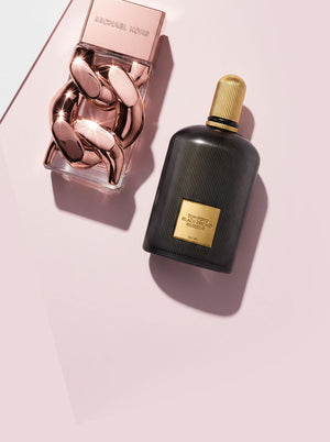 Michael Kors and Tom Ford perfume bottles on a soft pink background with luxury styling.