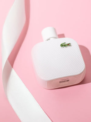 Lacoste white perfume bottle on a soft pink background with a white ribbon accent.